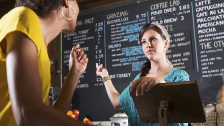 Mid adult woman (30s) working in restaurant, taking an order from an African American customer.