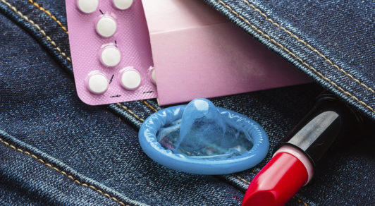 Healthcare medicine, contraception and birth control. Closeup oral contraceptive pills, condom and red lipstick in denim pocket.