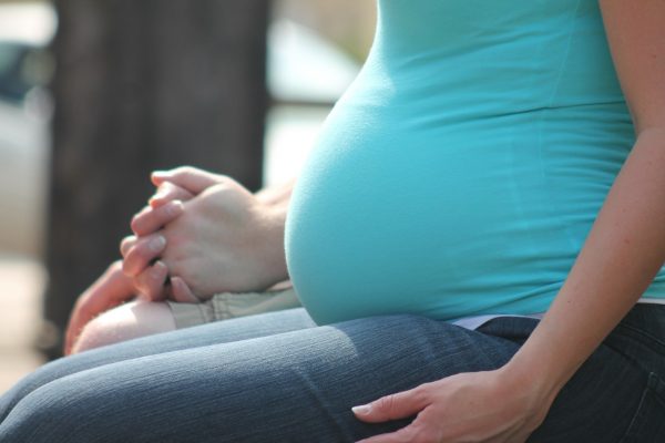 A pregnant person holds hands with someone while sitting down. 