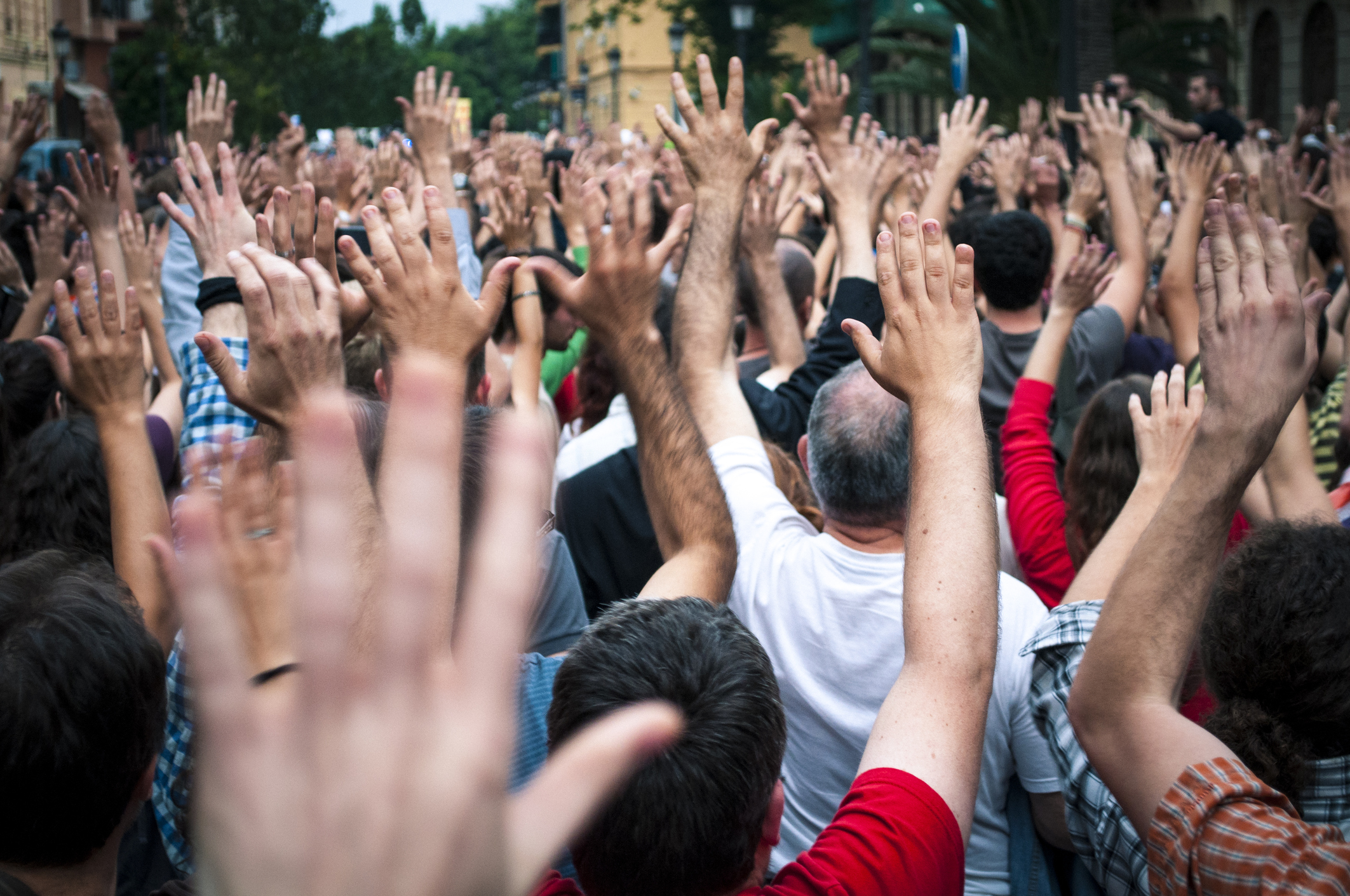 Image of a crowd of men outside having their backs turned to the camera and raising their hands.