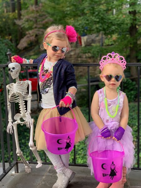 Two young girls pose with trick or treat baskets while wearing costumes.