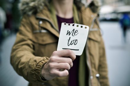 closeup of a young caucasian woman in the street showing a piece of paper with the text me too written in it