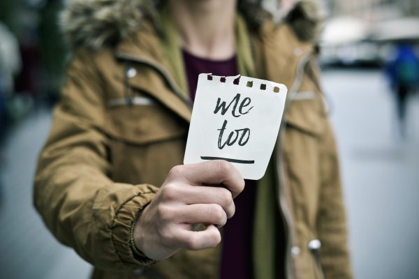 A young person holds up a note with "me too" written on it