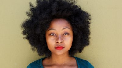 Close up serious young woman standing by wall with afro