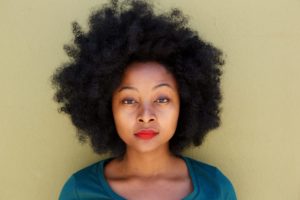 Close up serious young woman standing by wall with afro