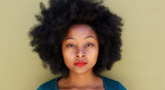 Close up serious young woman standing by wall with afro