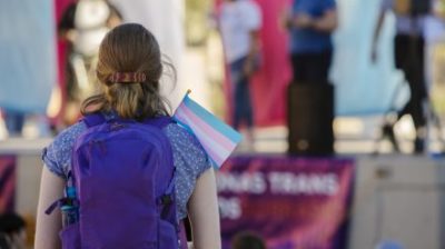 Young person with a backpack holding a transgender pride flag at rally