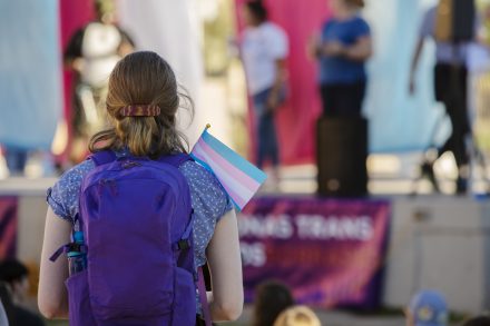 Young person with a backpack holding a transgender pride flag at rally