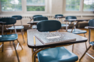 Empty desks in a classroom, one desk has a notebook and pencil