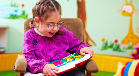cute girl in wheelchair playing with developing toy in kindergarten for children with special needs